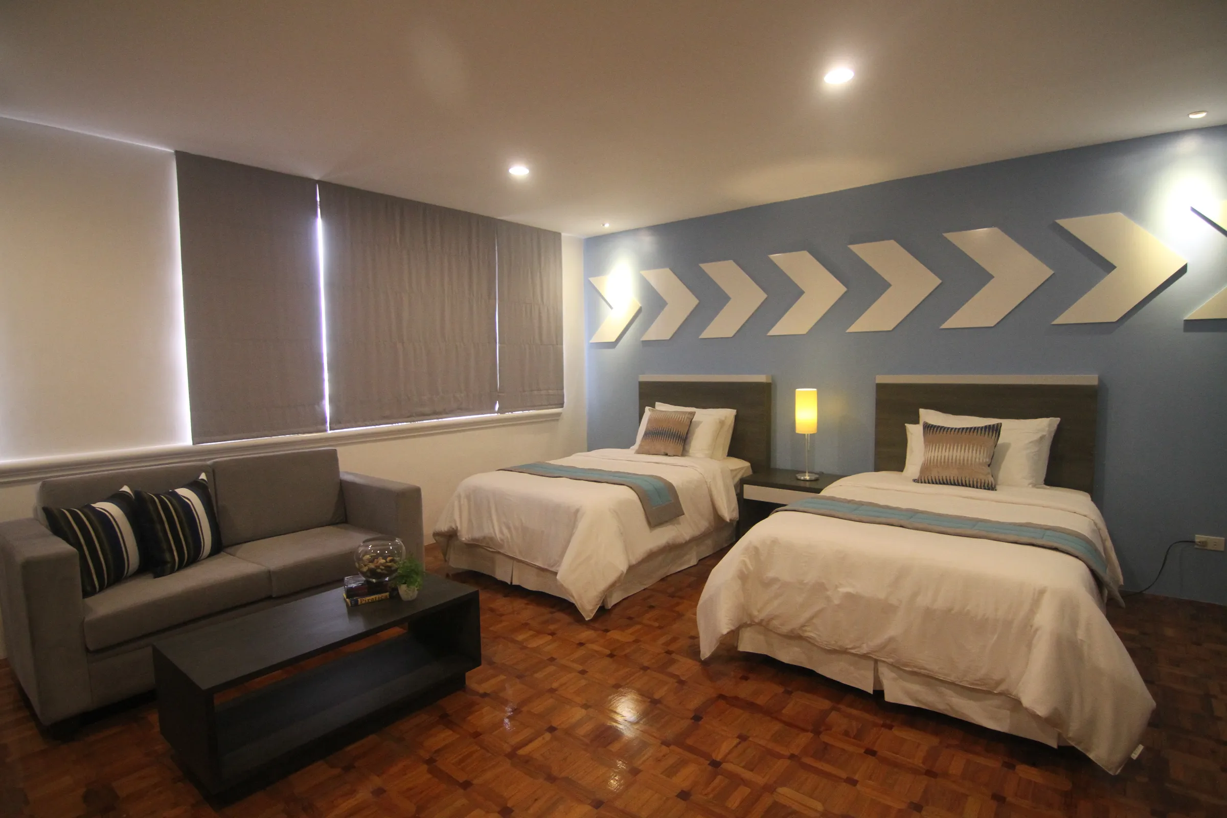 The Deluxe Twin room — two single beds with a sofa, bright windows and warm wood floors.